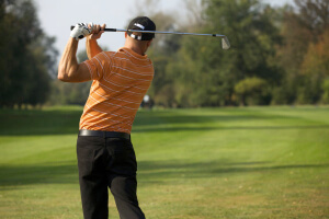 Rear of golfer demonstrating a simple golf swing as he hits the ball straight down the fairway